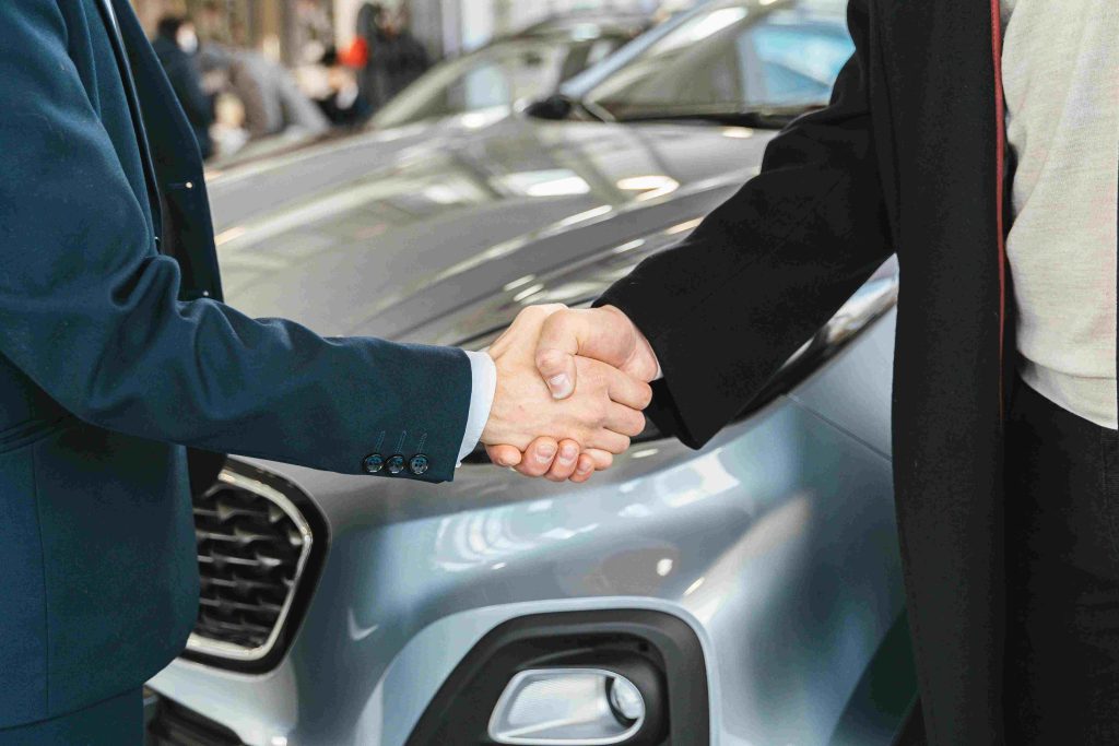 A close-up of two people in business attire shaking hands in front of a sleek car, symbolizing a professional agreement or partnership. ISP Companies