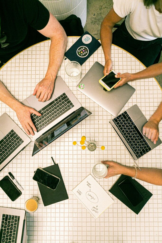 Overhead view of a team collaborating on laptops and smartphones at a round table, with notebooks and coffee cups.